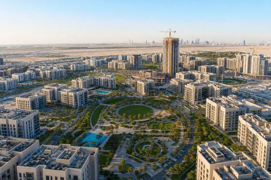Aerial view of a planned suburban residential community in Dubai showing mid-rise apartment towers arranged around circular parks and community pathways.